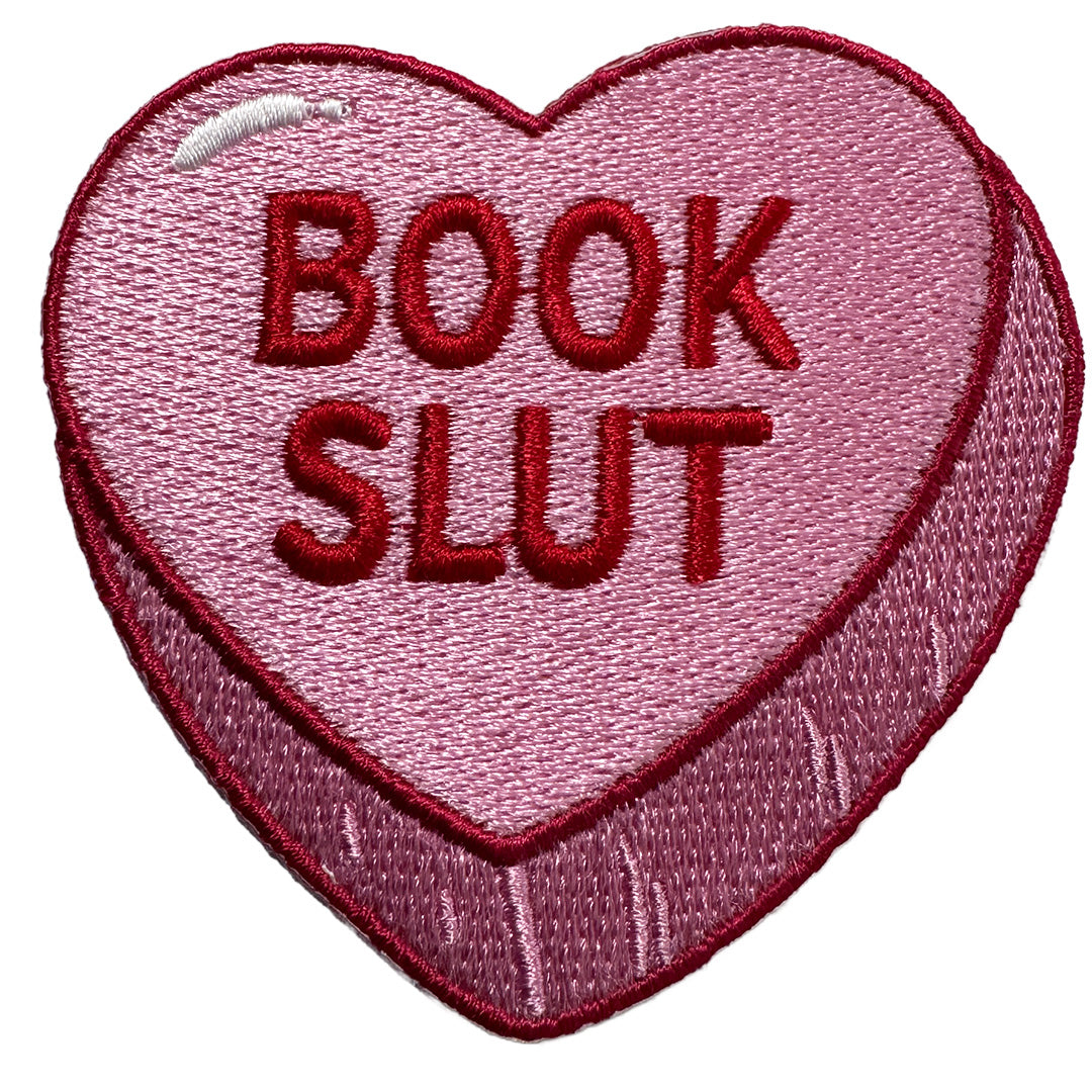 Heart-shaped patch with 'BOOK SLUT' text on a pink background
