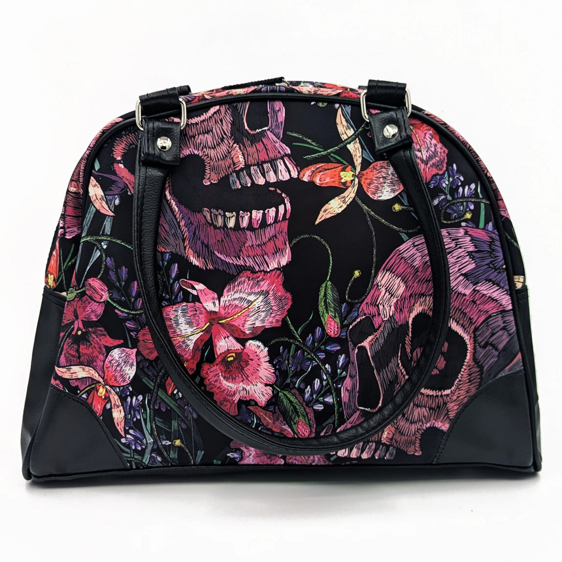 A black handbag with a floral and skull pattern, featuring a top handle and a front zipper.
